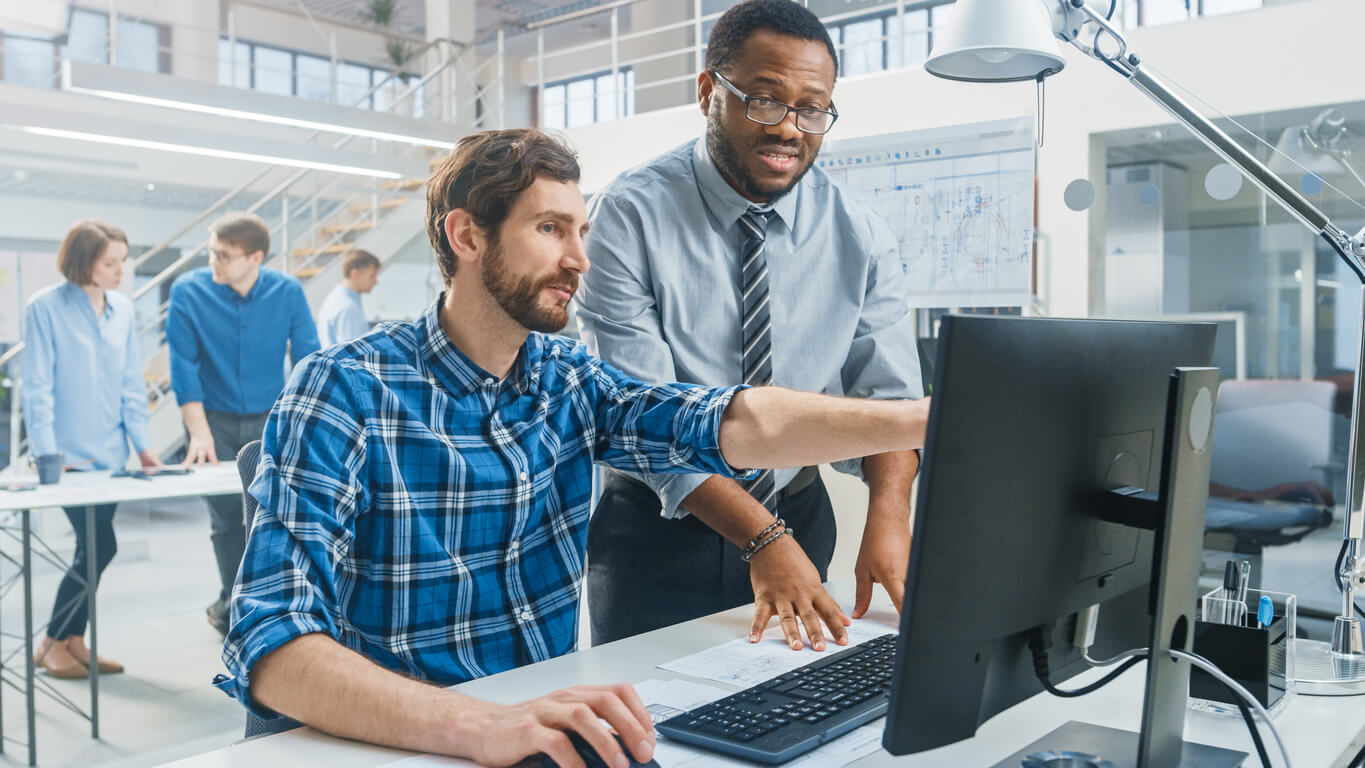 two male colleagues work at a desk looking at a black computer